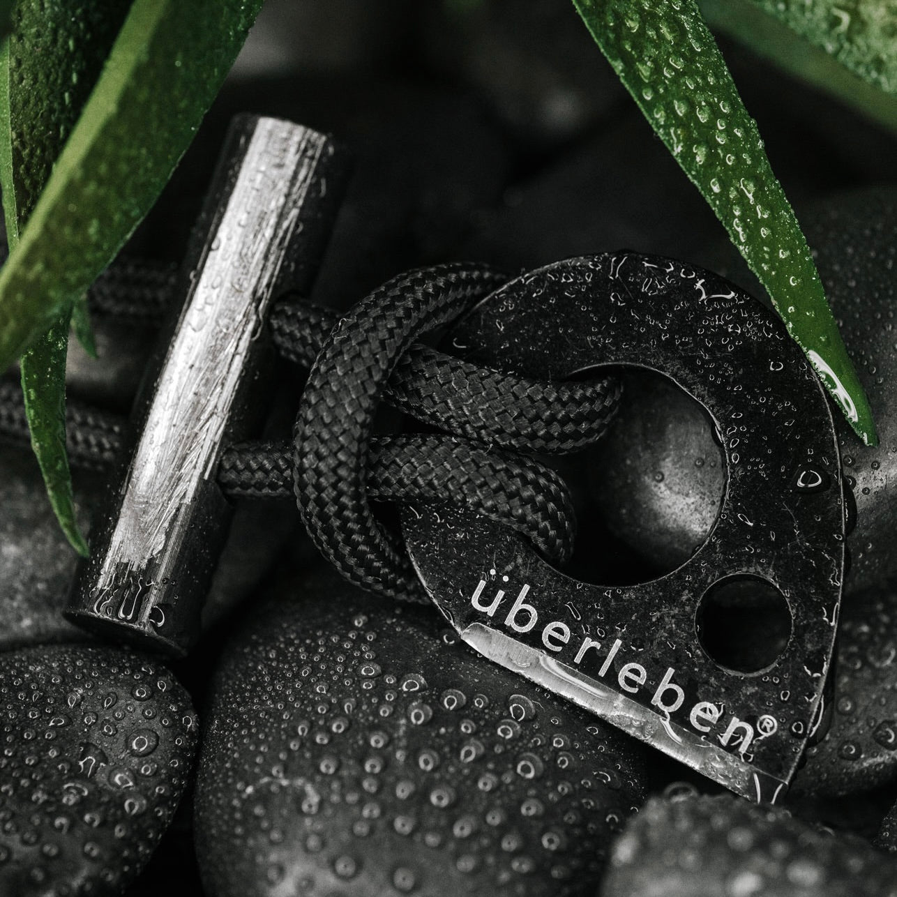 A close-up image of the Überleben Leicht, featuring a sleek black teardrop shaped striker secured to a black 550 paracord and accompanied by a short ferro rod.