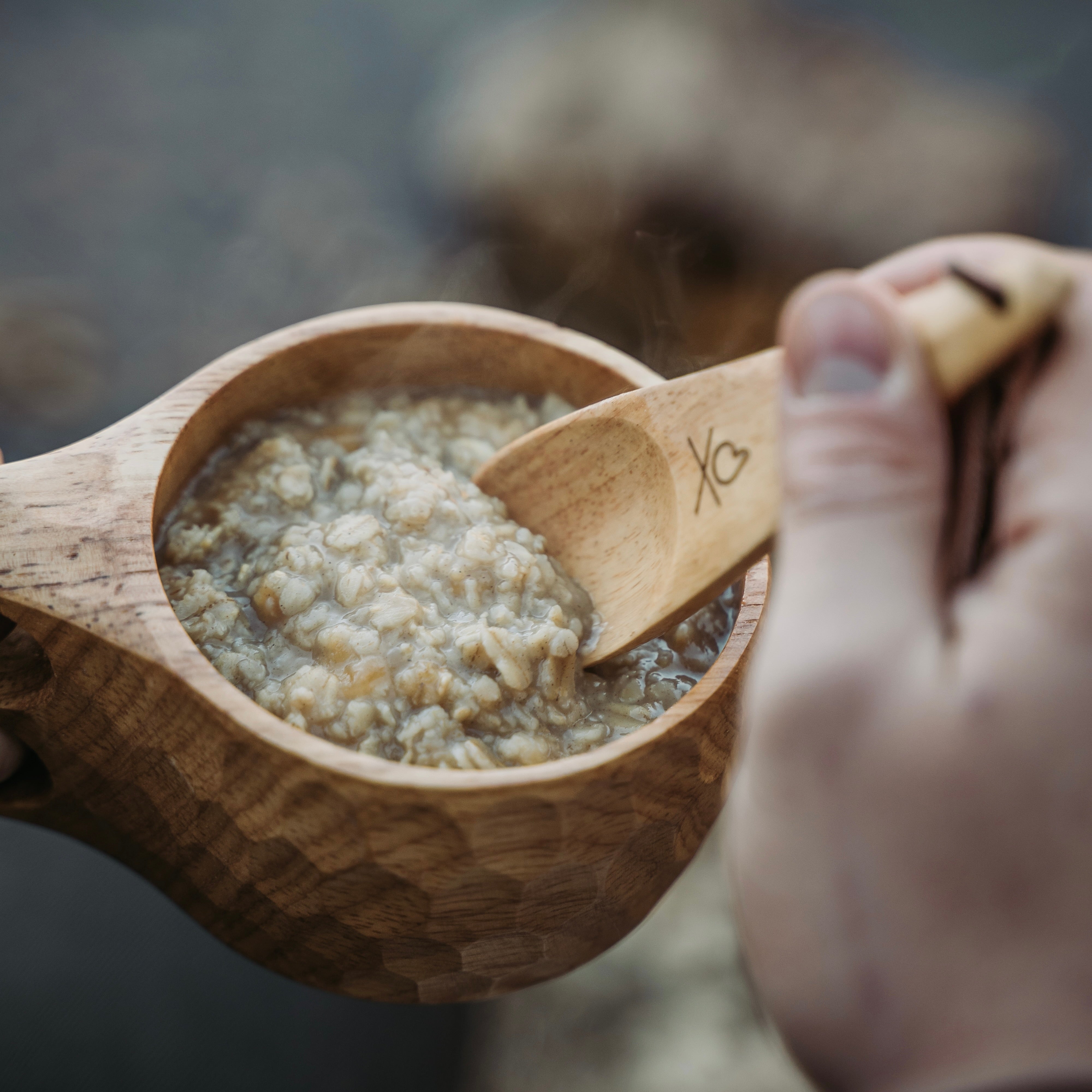 A person is eating oatmeal from Überleben's handcrafted Original 8oz Kuksa camp cup with a wooden spoon.